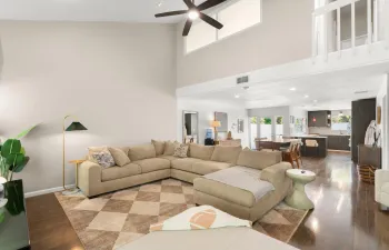 Living room with vaulted ceilings, large windows, and an open layout that flows into the dining area and kitchen.