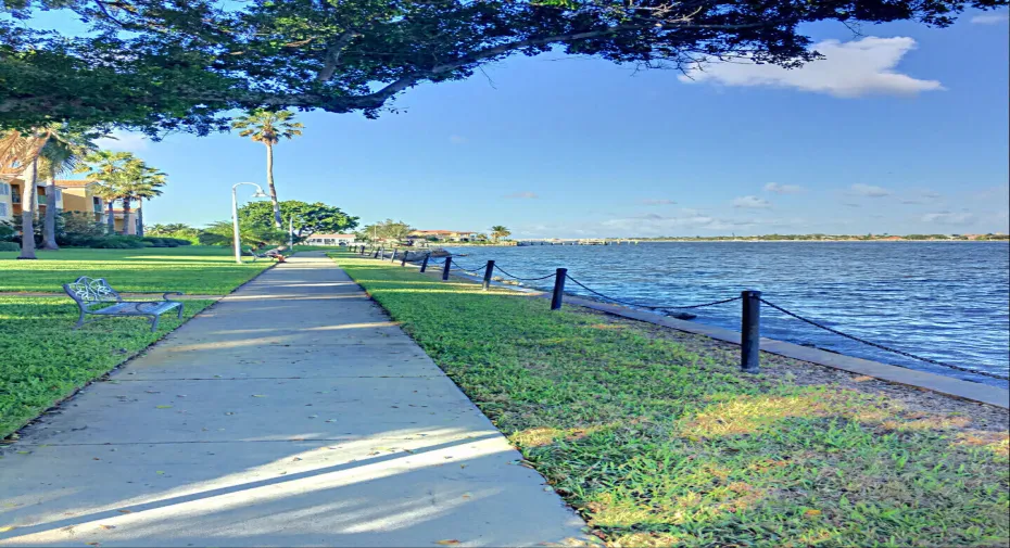 Waterfront concrete pathway featuring established trees and lush green space