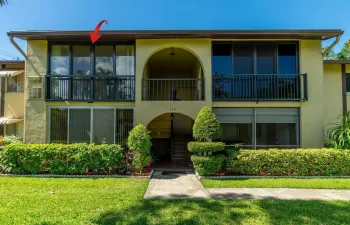 Two-story stucco building featuring a second-level balcony with black railing and multiple large windows