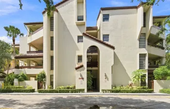 Front entrance to unit F, Spanish-tile roofline, arched breezeway, and mature landscaping with tropical foliage.