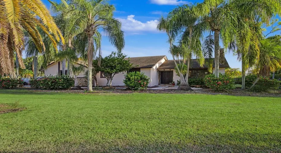 Single-story Redland home surrounded by mature tropical landscaping and a spacious front lawn.
