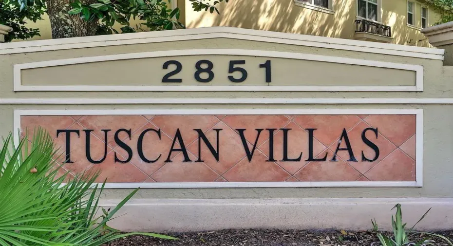 Entry monument featuring tan stucco, a prominent tiled sign with 