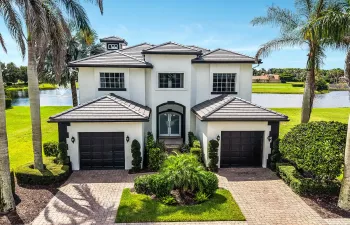 White stucco exterior with a tile roof, featuring a paver driveway, twin two-car garages, and mature palm trees