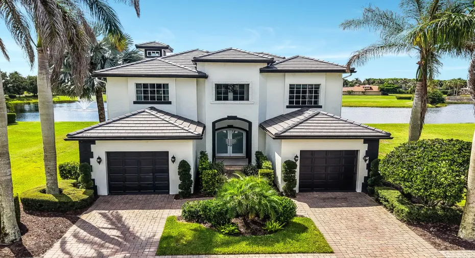 White stucco exterior with a tile roof, featuring a paver driveway, twin two-car garages, and mature palm trees