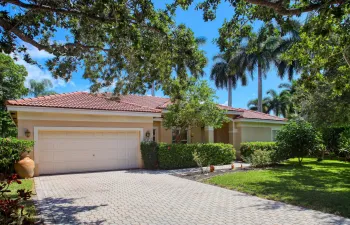 Beautiful front elevation featuring a tile roof, mature tropical landscaping, oversized driveway, and two-car garage in the desirable Yardley Estates community of Coral Springs.