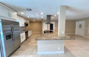 Kitchen featuring an island with a built-in cooktop and stainless steel vent hood, granite countertops, white cabinetry with silver hardware, stainless steel appliances, and tiled flooring
