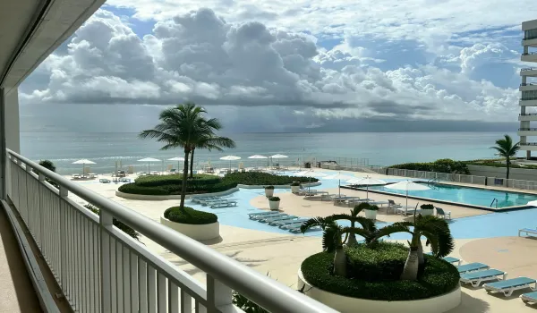 Expansive outdoor living area featuring a resort-style pool deck, multiple swimming pools, manicured landscaping with palm trees, and direct beach access