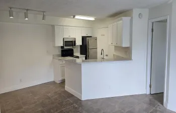 Open-concept kitchen featuring white cabinetry, stone-finish countertops, stainless steel appliances, and a breakfast bar