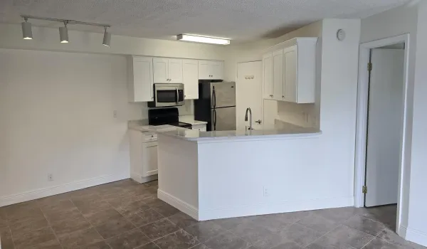Open-concept kitchen featuring white cabinetry, stone-finish countertops, stainless steel appliances, and a breakfast bar