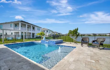 Expansive outdoor living area featuring a rectangular pool with an integrated spa, paver patio, and black metal fencing