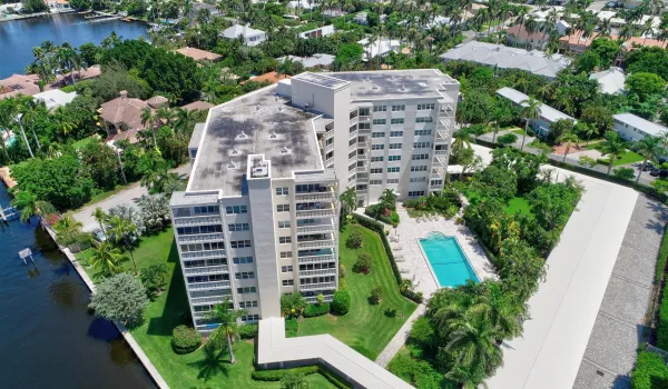 Waterfront mid-rise building, surrounded by green space, a rectangular swimming pool, and a paved parking area