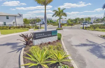 Gated community entrance featuring a stone-clad monument sign, mature palm trees, and landscaped grounds