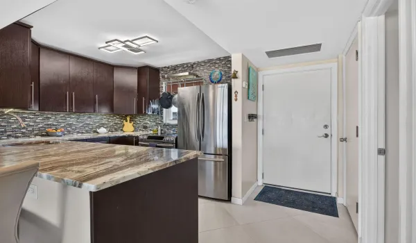 Kitchen featuring dark wood-finish cabinetry, patterned tile backsplash, stainless steel refrigerator, and light-toned countertop surfaces