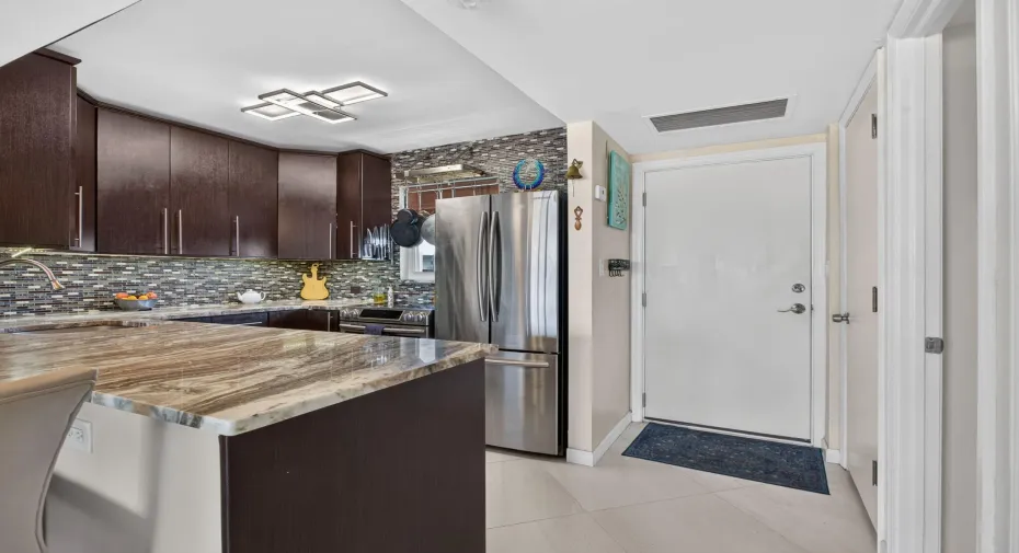 Kitchen featuring dark wood-finish cabinetry, patterned tile backsplash, stainless steel refrigerator, and light-toned countertop surfaces