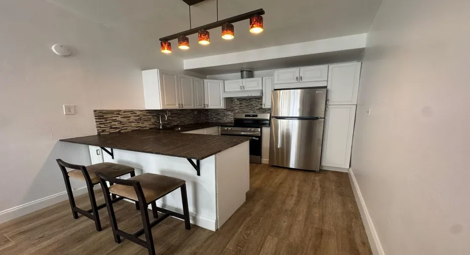 Contemporary kitchen featuring white cabinetry, stainless steel appliances, a mosaic tile backsplash, wood-finish flooring, and a breakfast bar with dark wood countertop