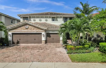 Two-story stucco and stone facade, tile roof, dual garage doors, paver driveway, and mature landscaping
