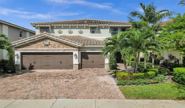 Two-story stucco and stone facade, tile roof, dual garage doors, paver driveway, and mature landscaping