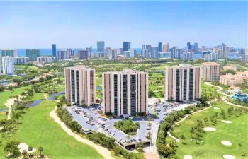 Three high-rise buildings situated amidst a golf course landscape with a distant city skyline and ocean background