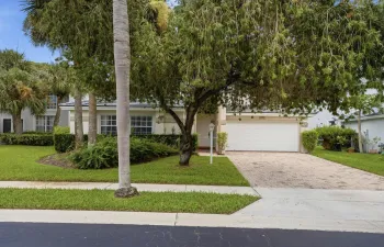 Paved driveway, white garage door, manicured lawn, established trees, and exterior lighting fixture
