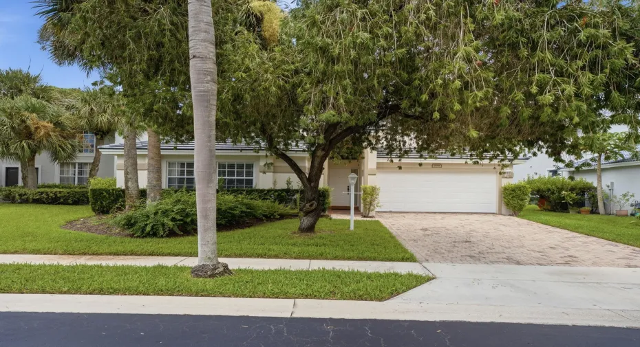 Paved driveway, white garage door, manicured lawn, established trees, and exterior lighting fixture