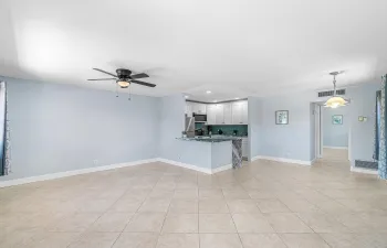 Spacious room with large format tile flooring, a ceiling fan, and a kitchen featuring white cabinetry, a tiled backsplash, stainless steel appliances, and a peninsula with a stone countertop