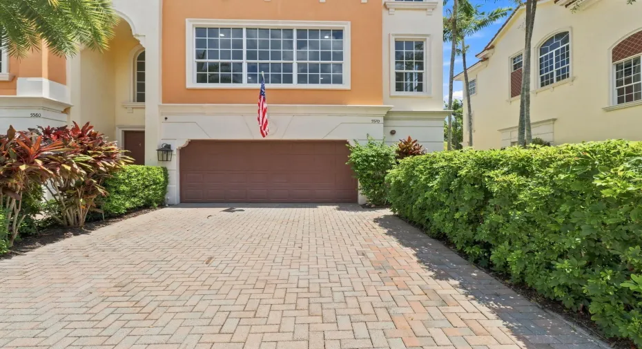 Paver driveway leading to an attached garage, featuring stucco exterior, arched entryways and ample fenestration