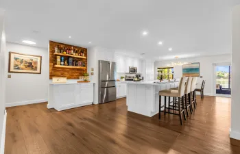 Wide plank wood-finish flooring, white cabinetry, stainless steel appliances, kitchen island with seating, and a built-in beverage bar with wood paneling