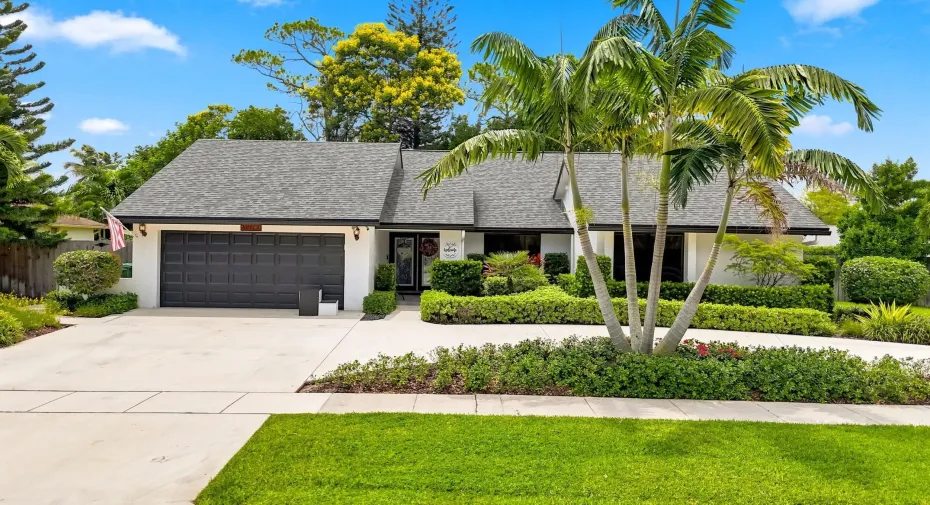 Beautifully landscaped front exterior with a spacious driveway, mature palms, and attached garage.