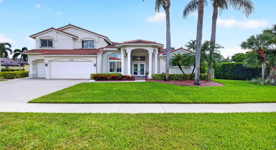 Mediterranean-style residence featuring a tile roof, stucco exterior, multiple palm trees, a three-car garage, and an arched entry with double doors