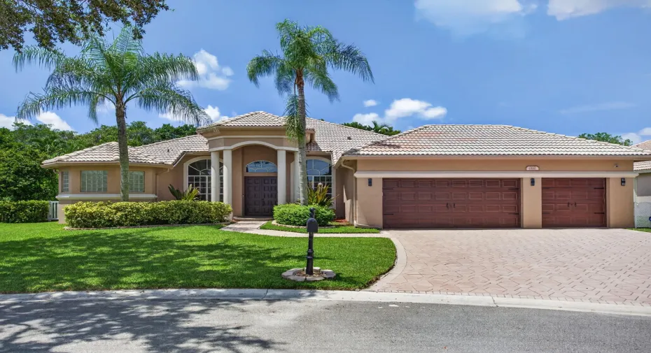 This home features a barrel tiled roof featuring a paver driveway, an arched entryway, mature palm trees and manicured landscaping.