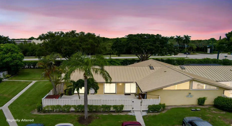 Property featuring a light-colored metal roof, private patio, lush green lawn, and mature palm trees
