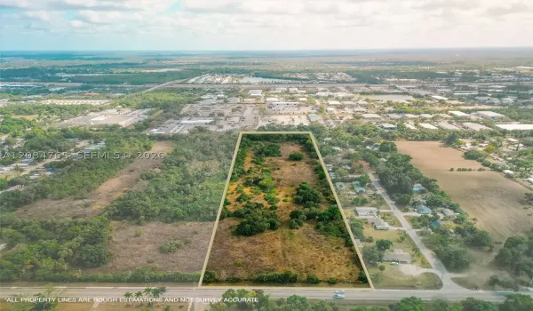 Stunning aerial drone view showcasing this vacant land parcel outlined amid mature trees, with easy paved road access and nearby residential development, a prime South Florida land investment opportunity.
