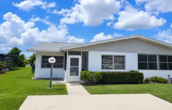 White exterior with stucco and vertical siding accents, featuring a screened entry and a well-maintained lawn