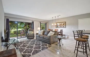 Spacious living area featuring wood-finish flooring, sliding glass doors, and a dining area with pendant lighting