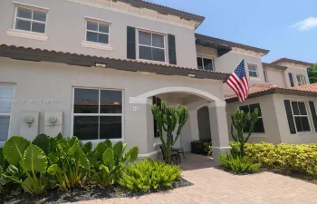 Charming two-story residence with a clean exterior and well-maintained details. Features a tiled roof, white-framed windows, and an elegant arched entrance leading to a tropical garden with tall succulents and ornamental plants. Located in a quiet and attractive condominium.