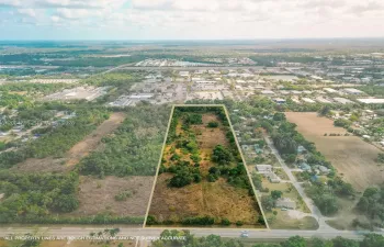 Stunning aerial drone view showcasing this vacant land parcel outlined amid mature trees, with easy paved road access and nearby residential development, a prime South Florida land investment opportunity.