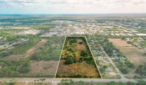 Stunning aerial drone view showcasing this vacant land parcel outlined amid mature trees, with easy paved road access and nearby residential development, a prime South Florida land investment opportunity.