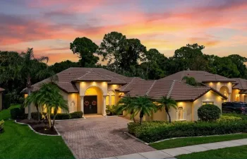 Tile roof, arched entryway, paver driveway, mature landscaping.