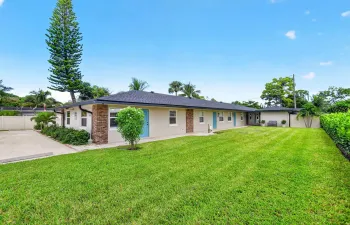 Expansive lawn with mature landscaping, a long paved driveway, brick accents, and vibrant blue entry doors