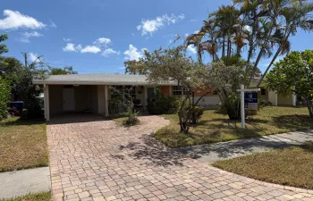 Single-story residence featuring a covered carport, brick paver driveway, and mature palm trees