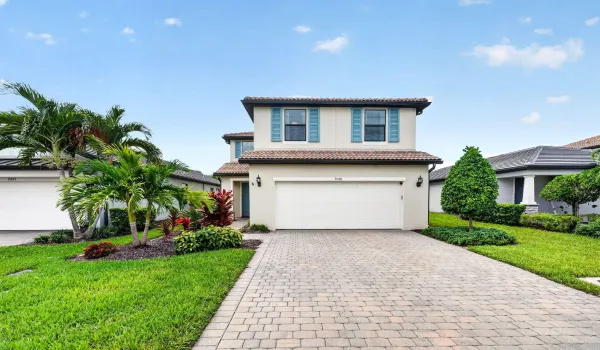 Two-story stucco exterior with decorative shutters, barrel tile roof, paver driveway, and an attached two-car garage