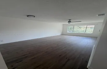 Open interior space featuring wood-finish flooring, a ceiling fan, a flush-mount light fixture, and a large picture window