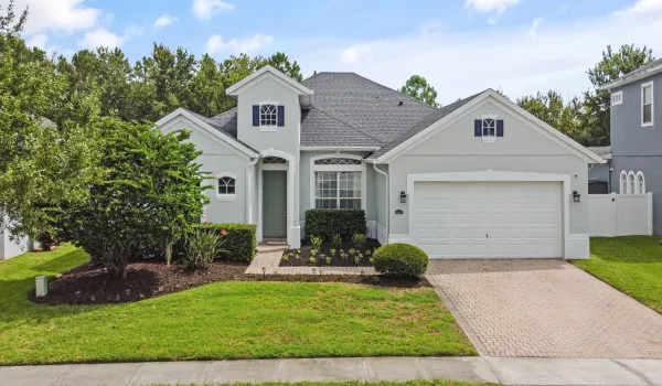 Stucco exterior with a dark shingle roof, arched entryway, a paver driveway, and an attached two-car garage