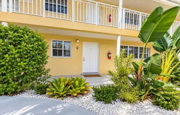 Tropical landscaping with white gravel accents, featuring a light yellow exterior and white architectural railings