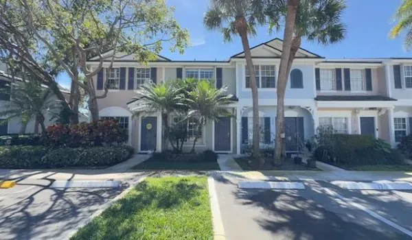 Two-story exterior with a pitched roofline, decorative window shutters, mature palm trees, and lush landscaping
