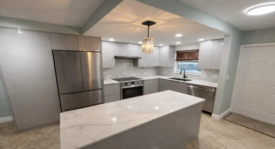 Kitchen featuring an island with a light-toned countertop, stainless steel appliances, light gray cabinetry, and a crystal pendant light