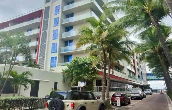 Mid-rise multi-story building featuring glass balcony railings, floor-to-ceiling windows, and red architectural accents
