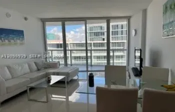 Floor-to-ceiling sliding glass doors opening to a balcony with metal railing, reflective tile flooring, and neutral wall finishes