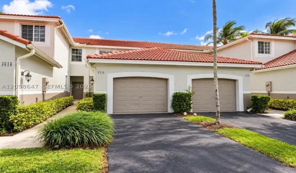 Beautiful two-story home with paving stone driveway, attached garage, and lush tropical landscaping.