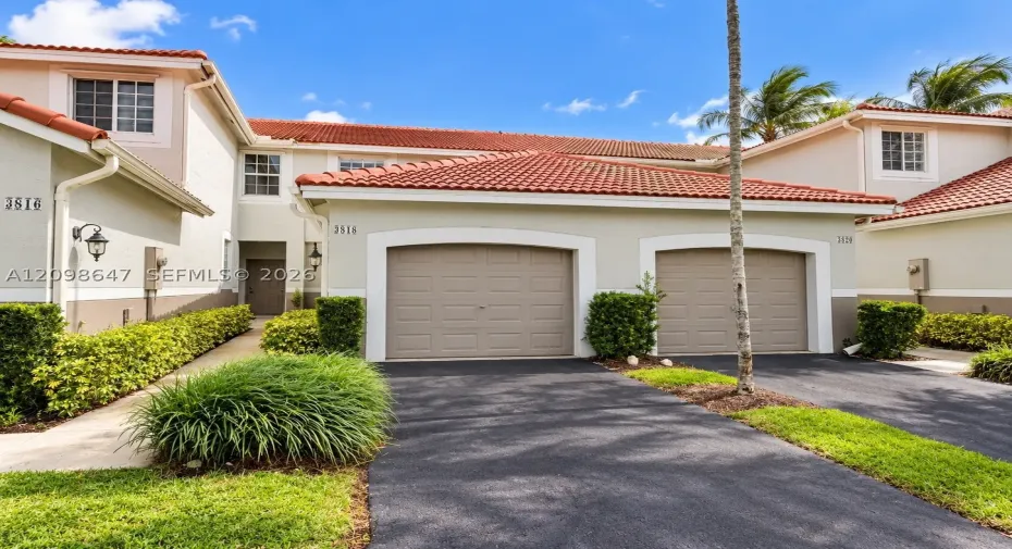 Beautiful two-story home with paving stone driveway, attached garage, and lush tropical landscaping.
